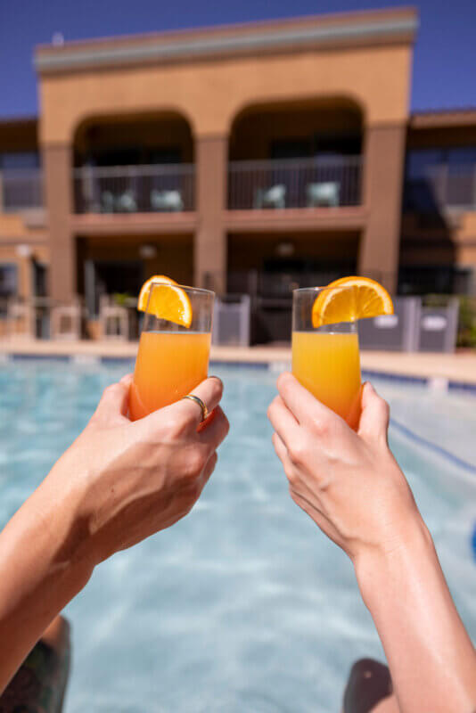 Two people drinking mimosas by the pool